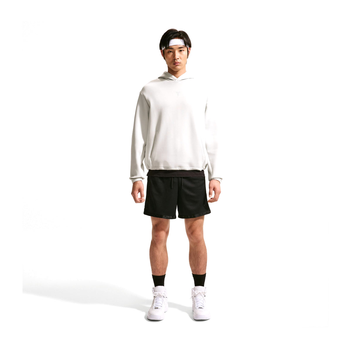 A man modeling a white long-sleeve athletic hoodie and black athletic shorts, standing against a solid white background.