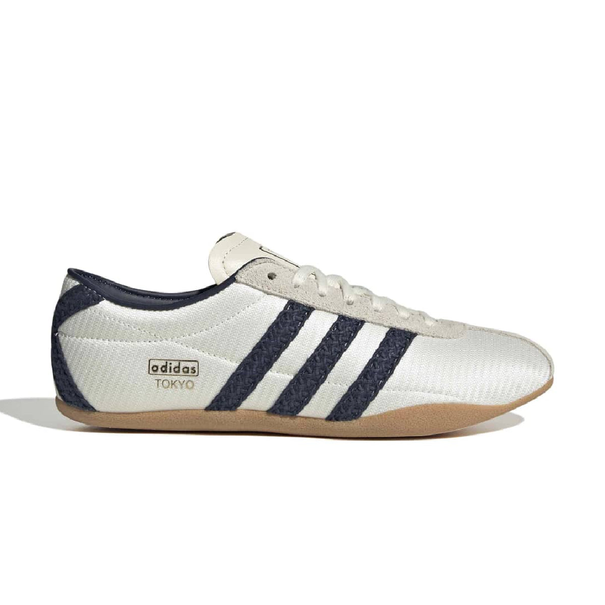 An Adidas Tokyo low-top sneaker in white and navy blue, featuring the signature three stripes on the side, a textured white upper, navy blue heel panel, and a brown gum sole, shown against a plain white background.