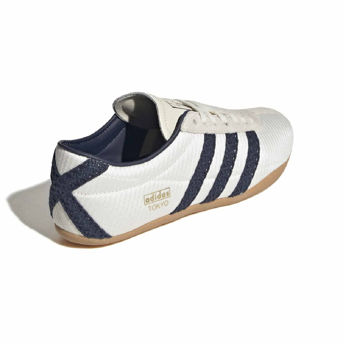 An Adidas Tokyo low-top sneaker in white textured canvas with navy blue glittery three-stripes, a navy blue heel accent, and a brown gum sole, shown from a three-quarters angle on a white background.