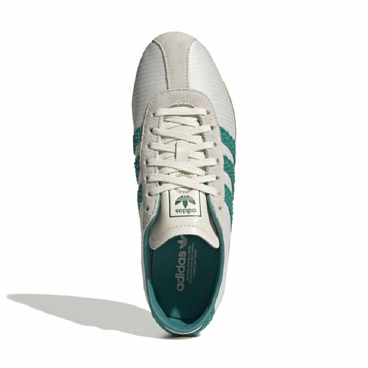 A single Adidas Tokyo sneaker shown from a top-down view on a white background. The shoe features a white leather upper with textured panels, white laces, and teal green accents on the side stripes, heel, and inner sole.