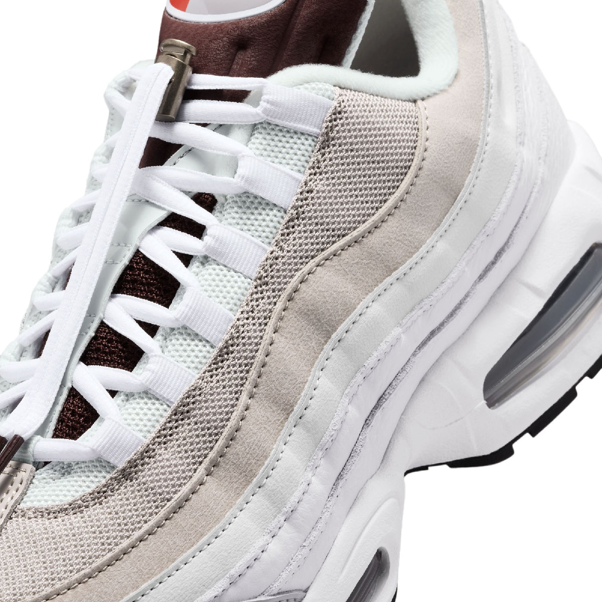 A close-up of a chunky sneaker featuring a mix of white mesh, light beige suede, and dark brown accents, with white laces and a thick white sole.