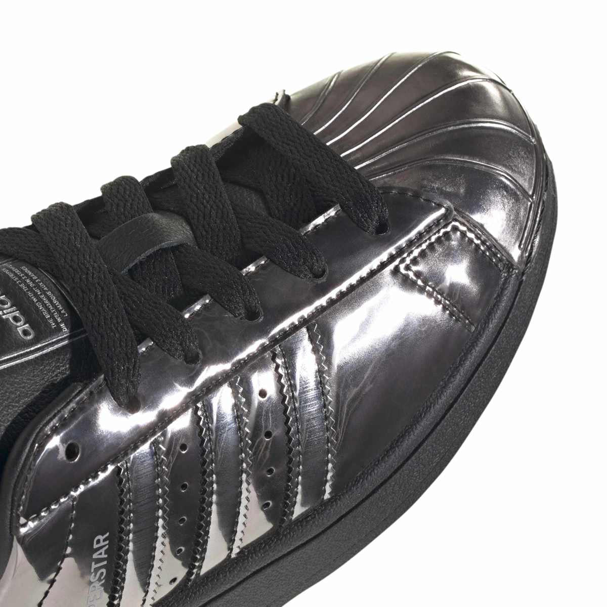 A close-up of a metallic silver Adidas Superstar sneaker with black laces and a black sole, set against a plain white background.
