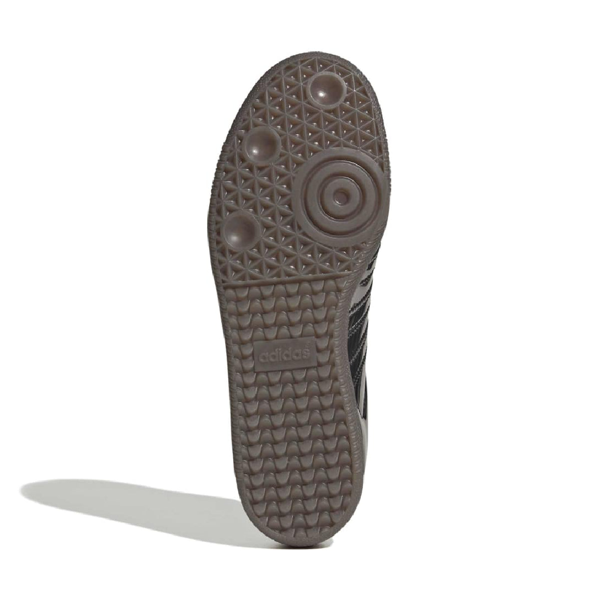 The outsole of a dark brown Adidas sneaker, showing the textured tread pattern and embossed 'adidas' logo, photographed on a white background with a soft shadow.