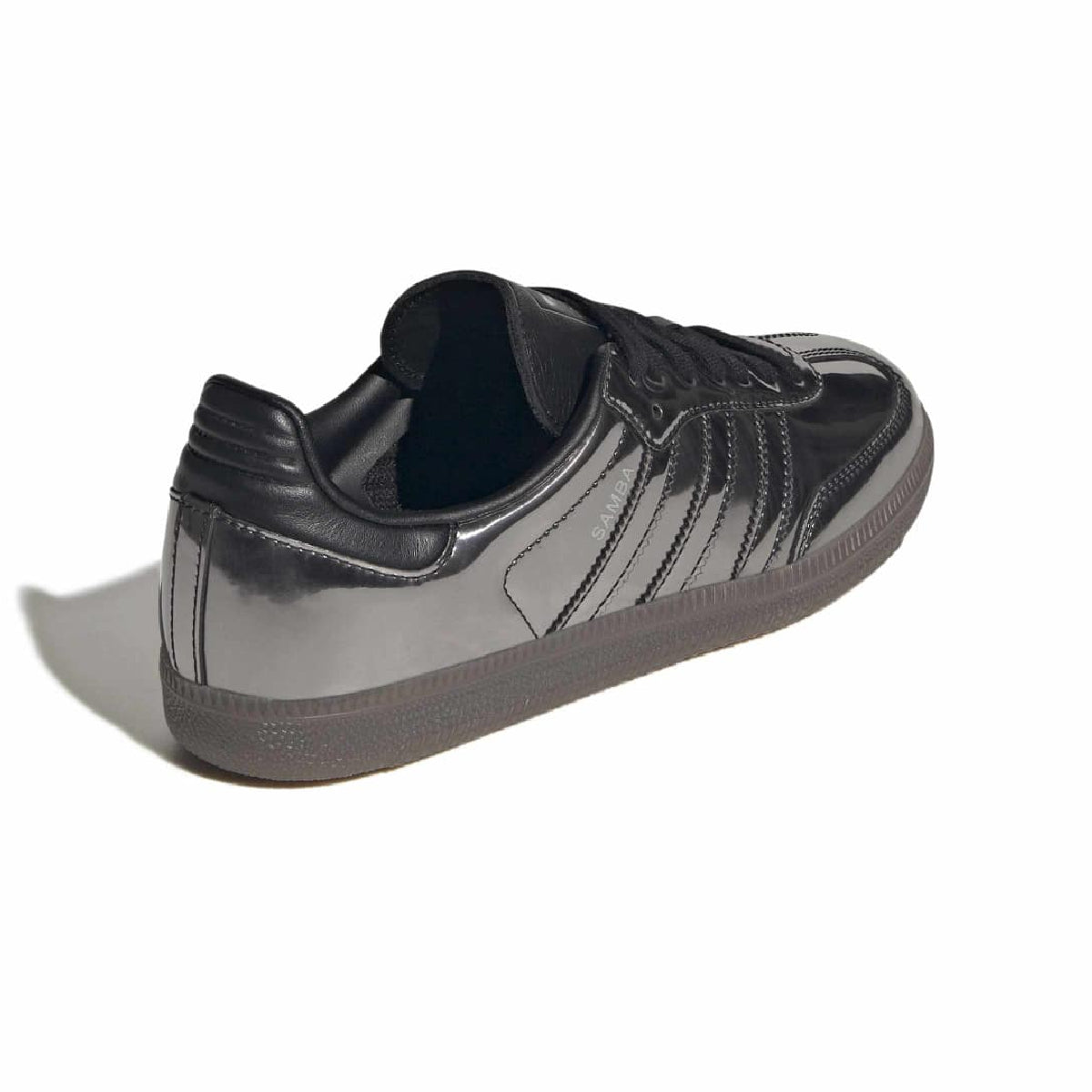 A low-top sneaker in glossy black patent leather with black laces and a dark gray rubber sole, shown from a three-quarters angle on a white background.