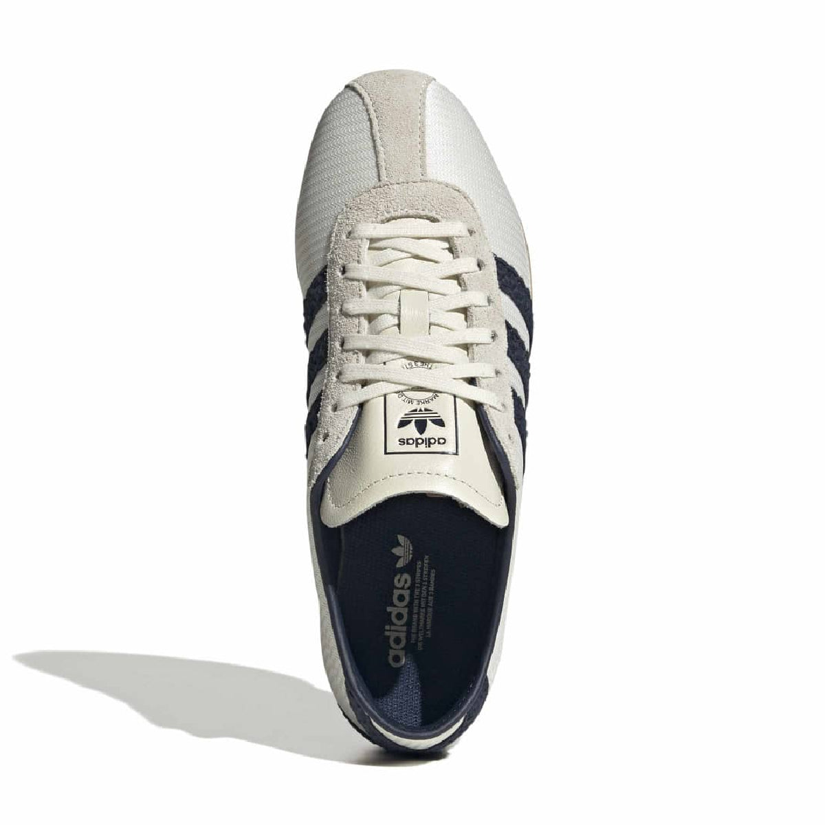 A single Adidas Tokyo sneaker shown from a top-down angle on a white background. The shoe features a cream and white leather upper with navy blue three-stripes, a cream tongue label, and a navy blue insole.
