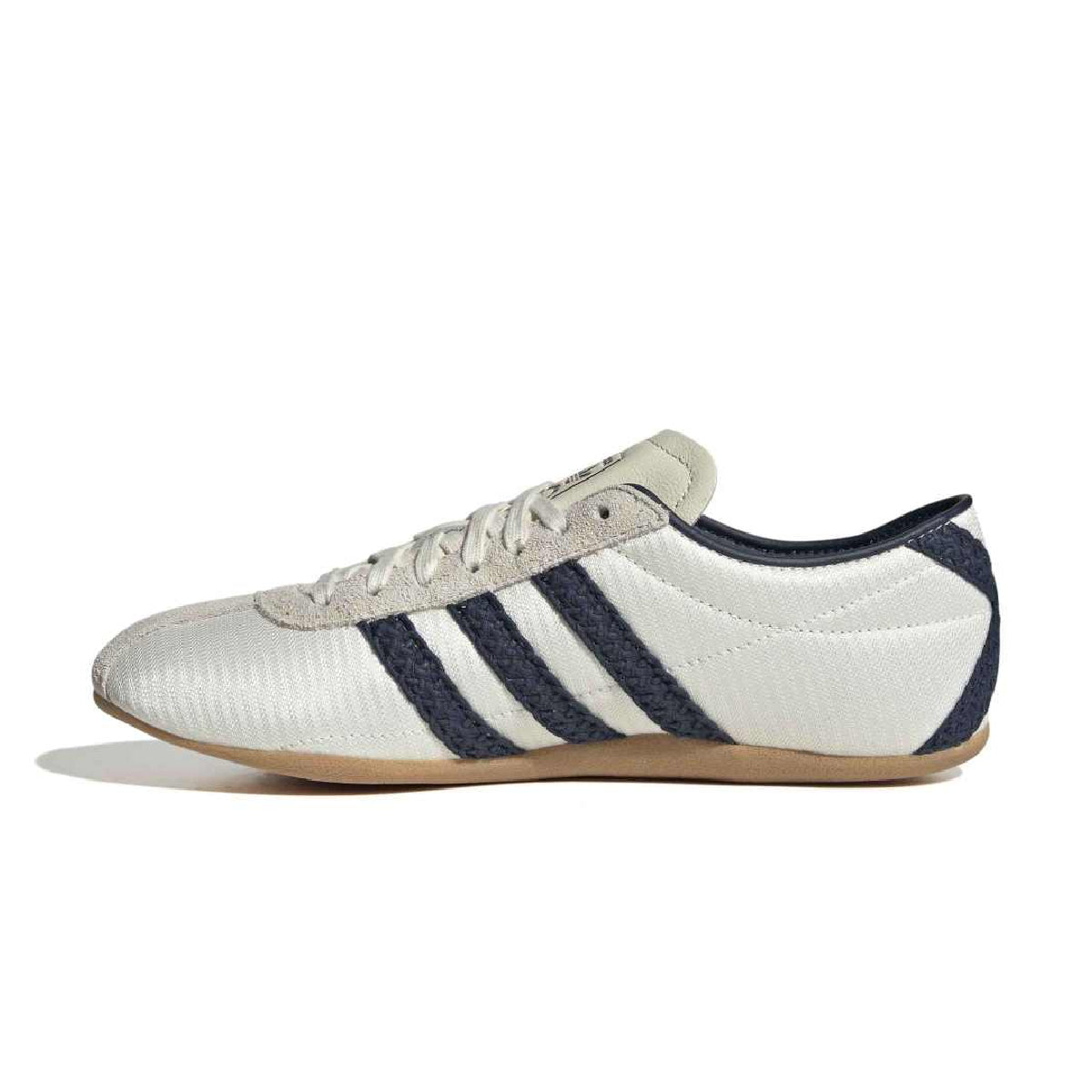 A white low-top sneaker with three dark navy stripes on the side, a beige tongue label, and a gum brown sole, shown in profile against a white background.
