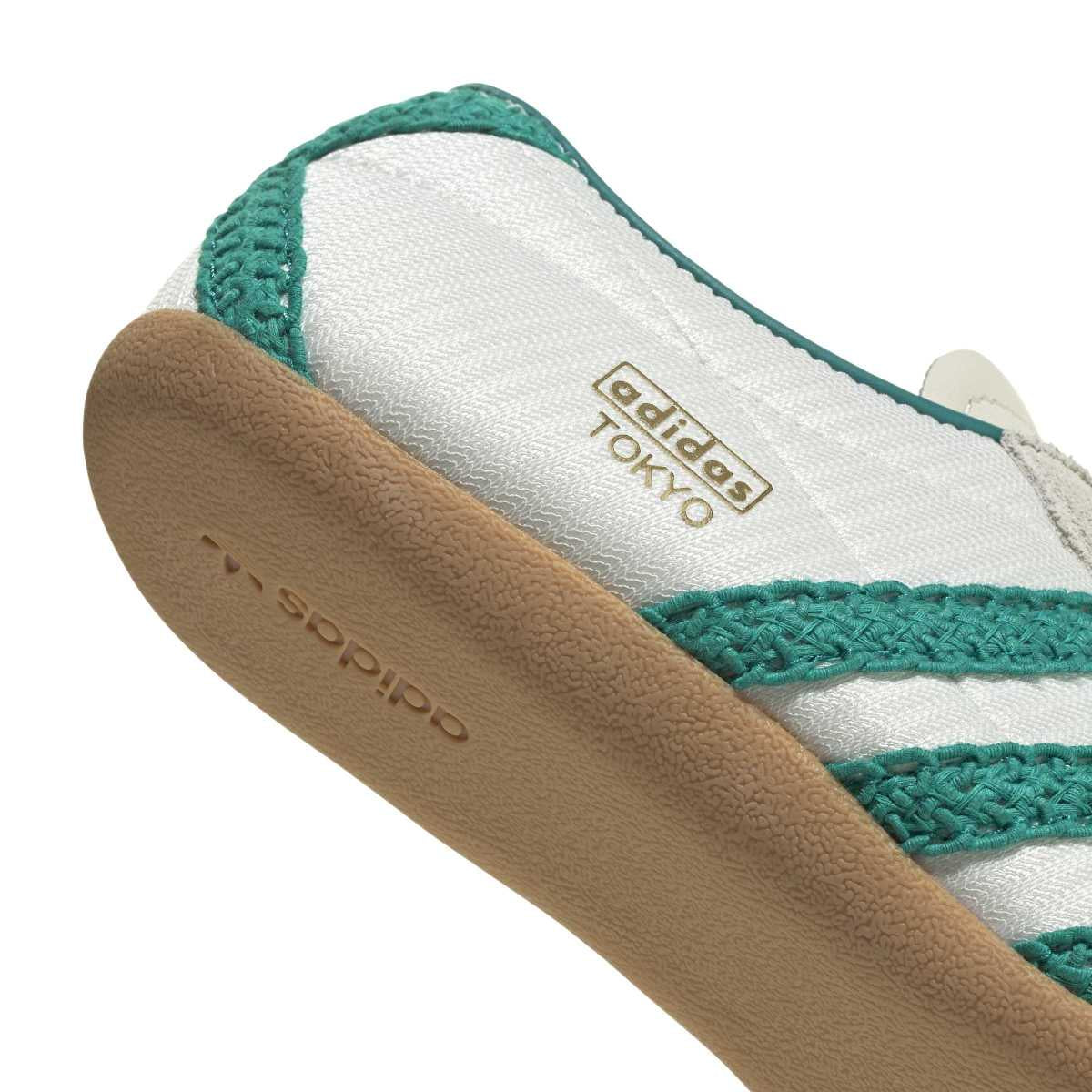 Close-up of an Adidas Tokyo sneaker showing the white textile upper, teal knit trim, and tan gum sole with embossed Adidas branding.