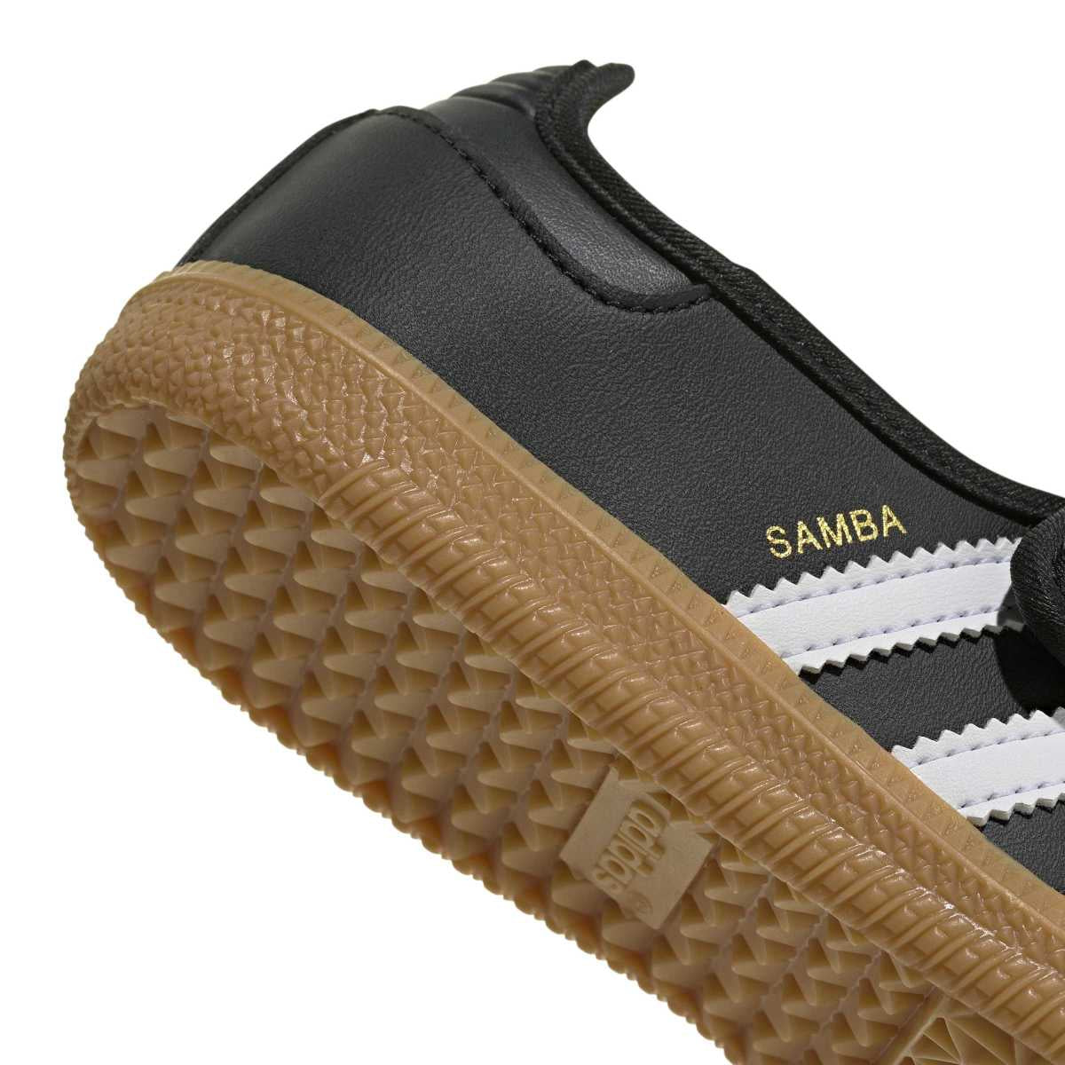 Close-up of a Samba shoe showing the black leather upper, white side stripes, gold 'SAMBA' text, and a tan gum rubber sole on a white background.