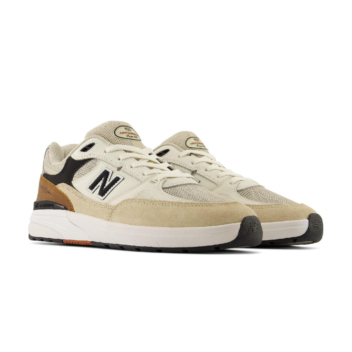 A pair of New Balance 933 sneakers in a light beige and cream colorway, featuring black and brown accents on the heel and toe, with a white midsole.